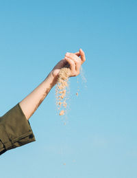 Cropped hand holding sand against blue background