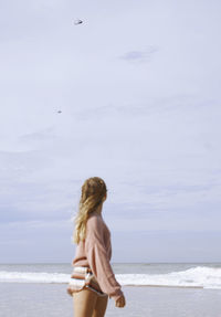 Teenage girl looking at helicopters flying over coastal beach