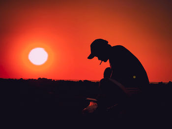 Side view of silhouette man sitting against orange sky at sunset