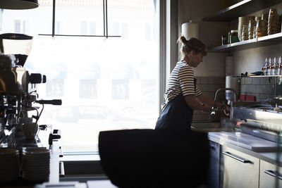 Side view of barista washing coffee filter at sink by window in cafe