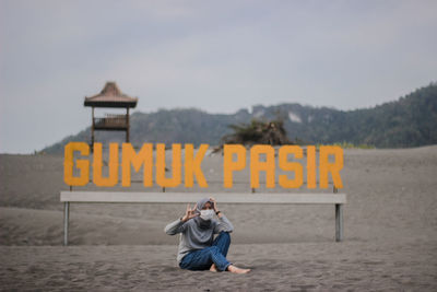 Full length of woman sitting on sand against advertisement