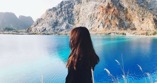 Rear view of woman standing by lake against mountain