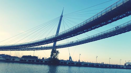 Low angle view of suspension bridge over river during sunset