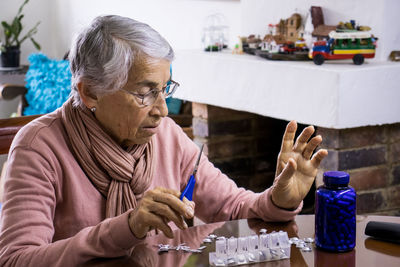 Senior woman taking medicine while sitting by table at home