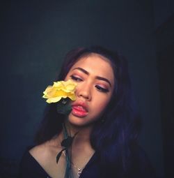 Close-up of young woman with yellow flower against wall