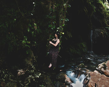 Full length of woman sitting on swing over river in forest