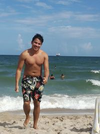 Full length of shirtless man standing at beach against sky