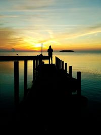 Silhouette of people standing on pier at sunset