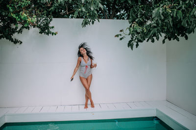 Full length of woman with arms raised against wall