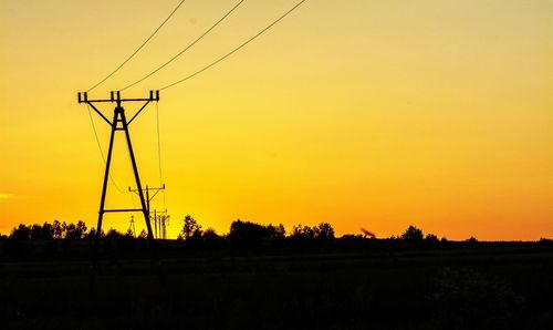 Silhouette of electricity pylons on landscape at sunset