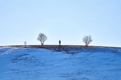 Rear view of mature man standing on snow covered field against clear sky