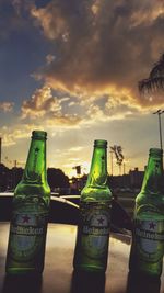 Close-up of beer bottles against sky during sunset