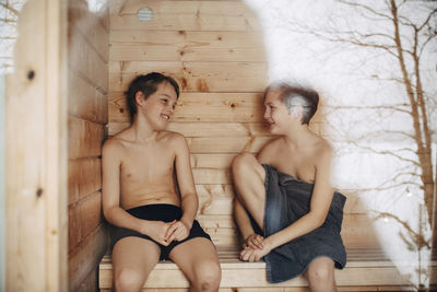 Smiling shirtless boys talking with each other while sitting in sauna