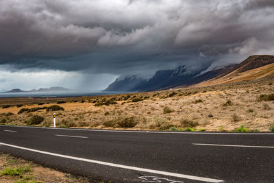 Road by mountain against cloudy sky