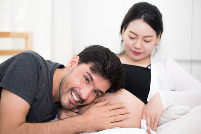 Young man listening to pregnant woman sitting on bed at home