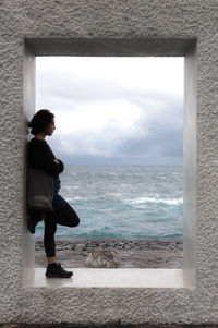 Side view of woman standing in built structure by sea against sky