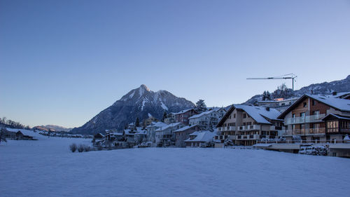 Houses by frozen lake against clear blue sky