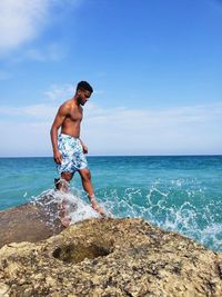 Full length of shirtless man standing at beach against sky