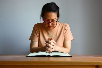 Asian christain woman praying while holding wood cross in front of the bible