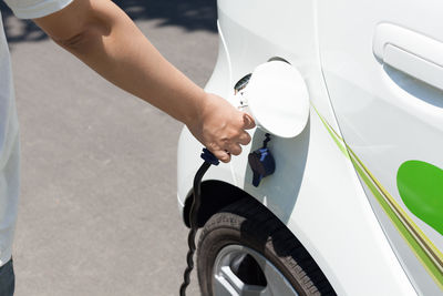 Cropped hand of person charging white electric car