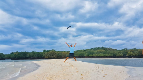 Man jumping at beach against sky