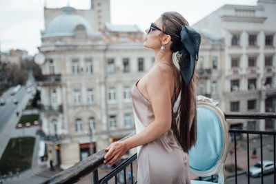 Side view of young woman standing on railing in city