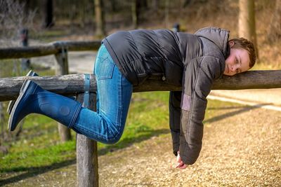 Portrait of boy lying on wooden railing at park