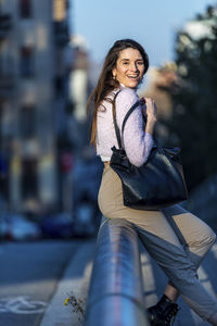 Portrait of smiling woman sitting on railing in city