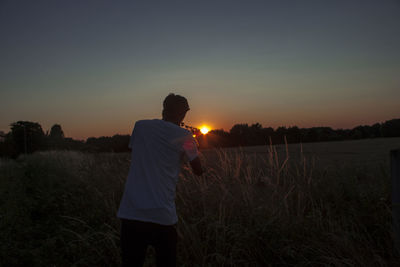 Rear view of boy standing on field against sky during sunset