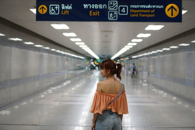 Rear view of woman standing under information sign at subway station