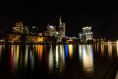 Illuminated buildings by river against sky at night