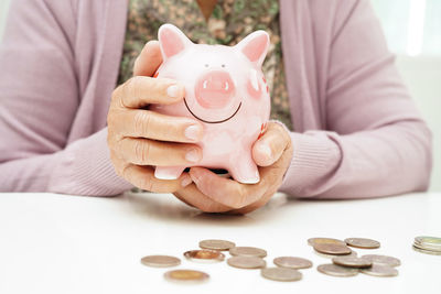 Midsection of woman putting coin in piggy bank
