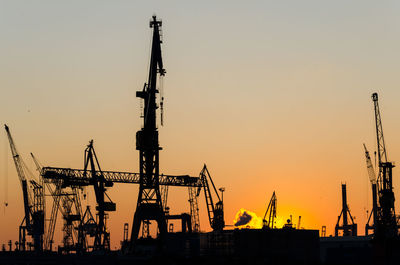 Silhouette cranes at commercial dock against sky during sunset
