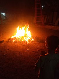 Rear view of boy standing by illuminated bonfire at night