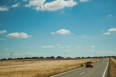 Road passing through field against sky