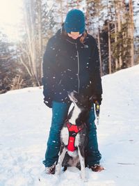 Woman with dog standing on snow against trees