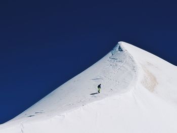 Person skiing on snow covered mountain against clear blue sky