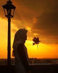 Side view of silhouette woman standing on street against sky during sunset