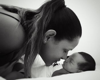 Mother rubbing cute daughter nose sleeping on bed