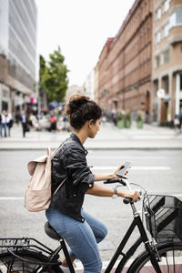 Woman looking at phone while riding bicycle on city street