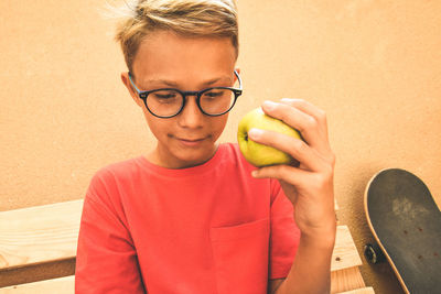 Boy holding apple while looking down against wall
