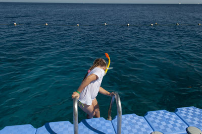A little girl in a white t-shirt and a swimming mask dives and swims in blue sea