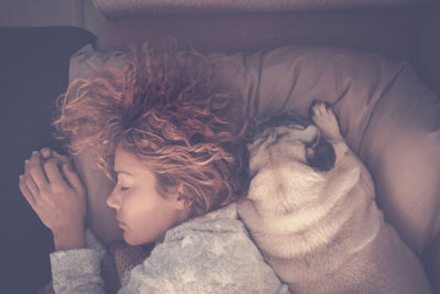 Directly above view of woman sleeping with dog on bed at home