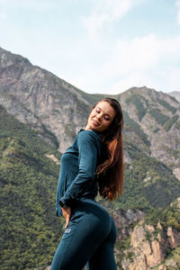 Side view of beautiful woman standing against mountain range