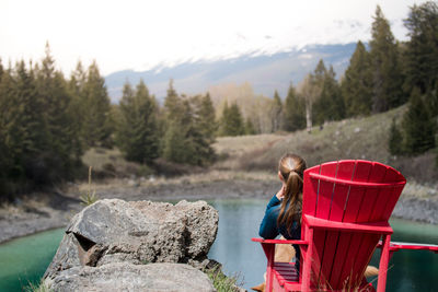 Rear view of woman sitting on chair against lake