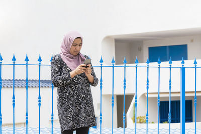 Muslim woman leaning on a metal fence checking her phone