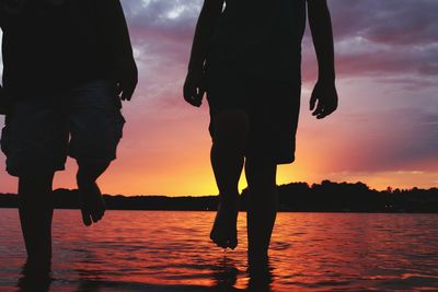 Low section of silhouette friends against sea during sunset