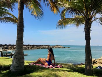 Young woman sitting on tree by sea against sky