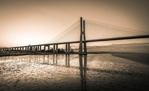 Bridge over calm river against sky during sunset