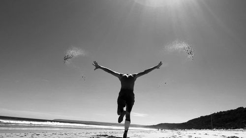 Man with arms raised on beach against sky